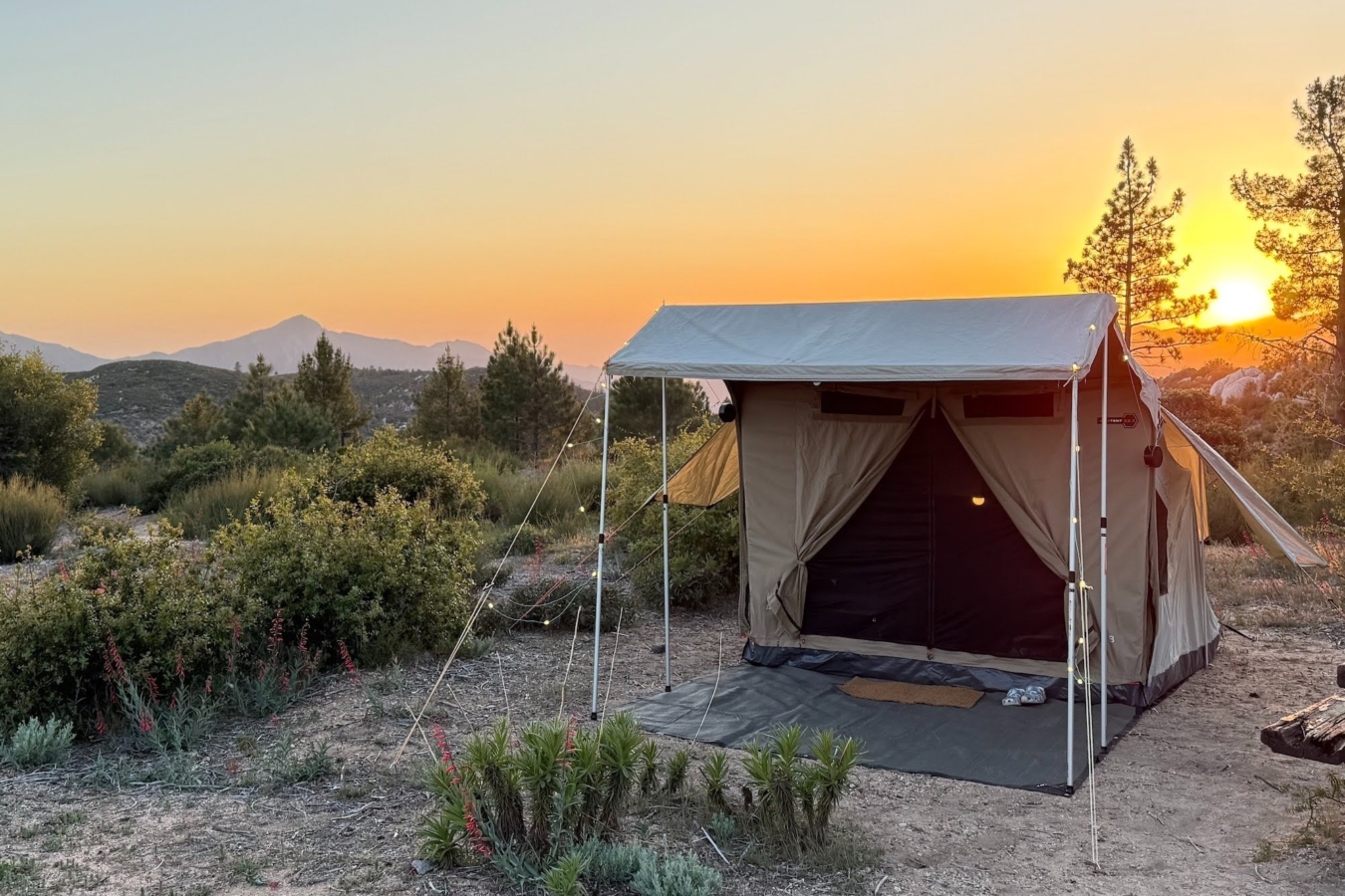 A tan tent is set up in front of a sunset.