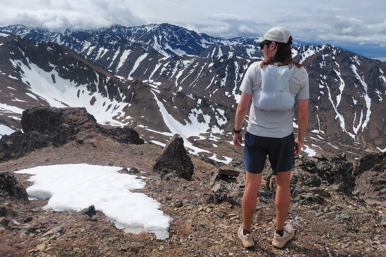 Runner wearing a white running vest while overlooking snow-covered mountains