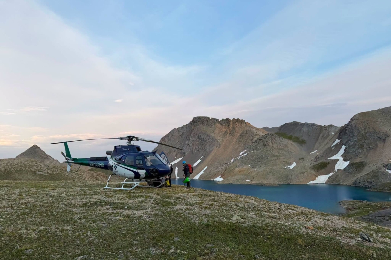 person stands next to helicopter in mountains