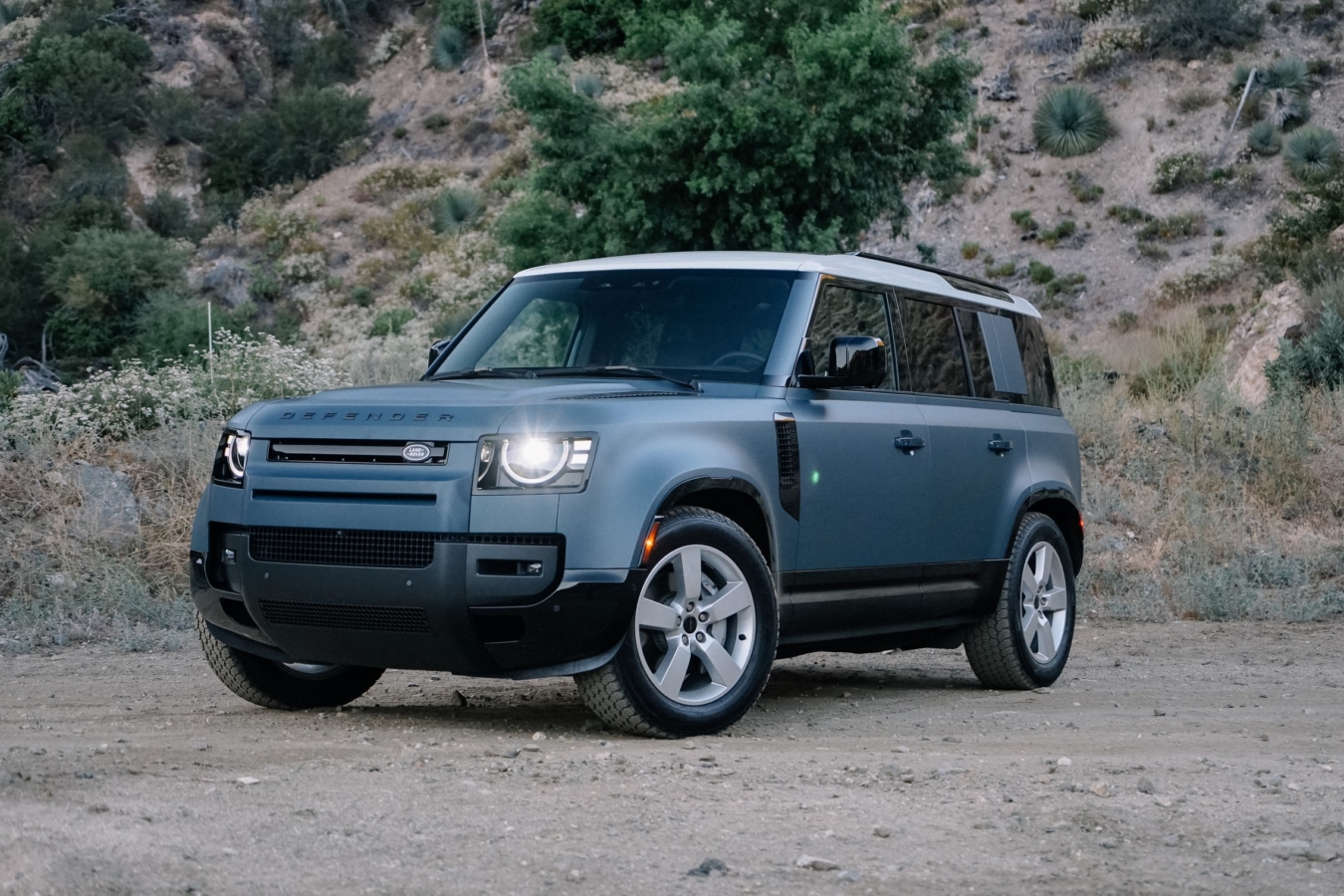 A matte blue 2026 Land Rover Defender 110 is parked on dirt