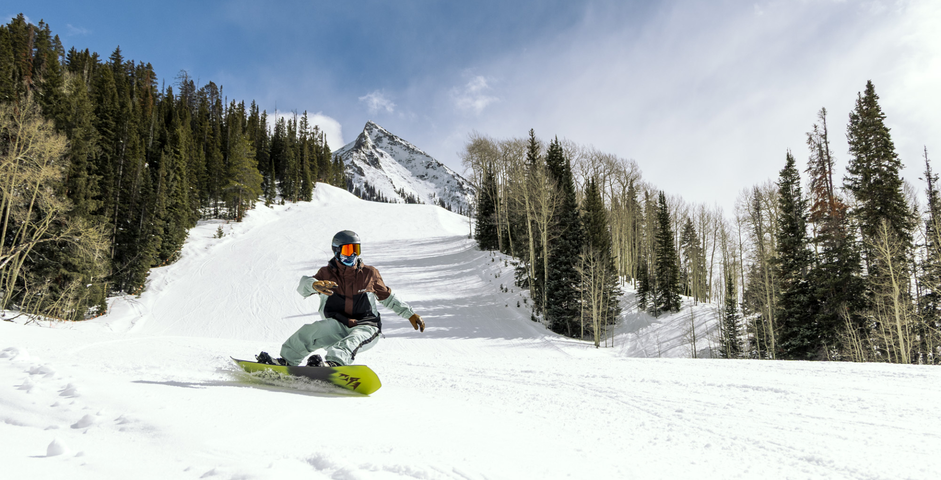 snowboarder on heel side edge with mountain and slope in background