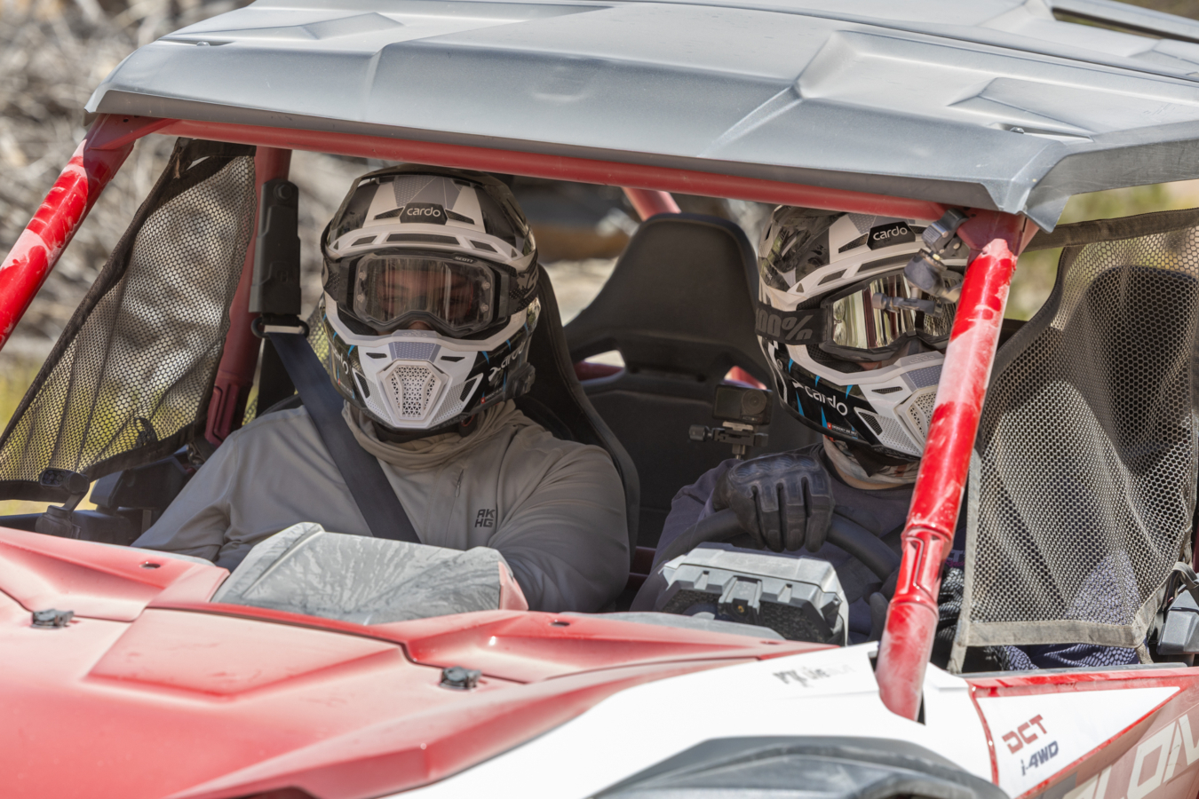 Two men in helmets sit in a red Honda UTV