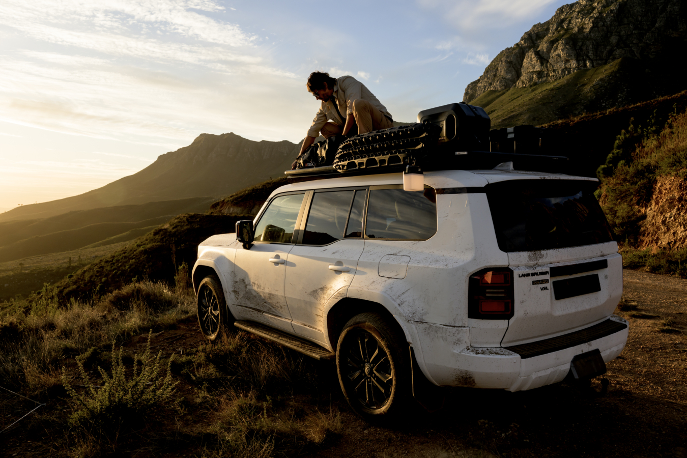 A man is strapping something to the roof rack on his white Toyota Land Cruiser.