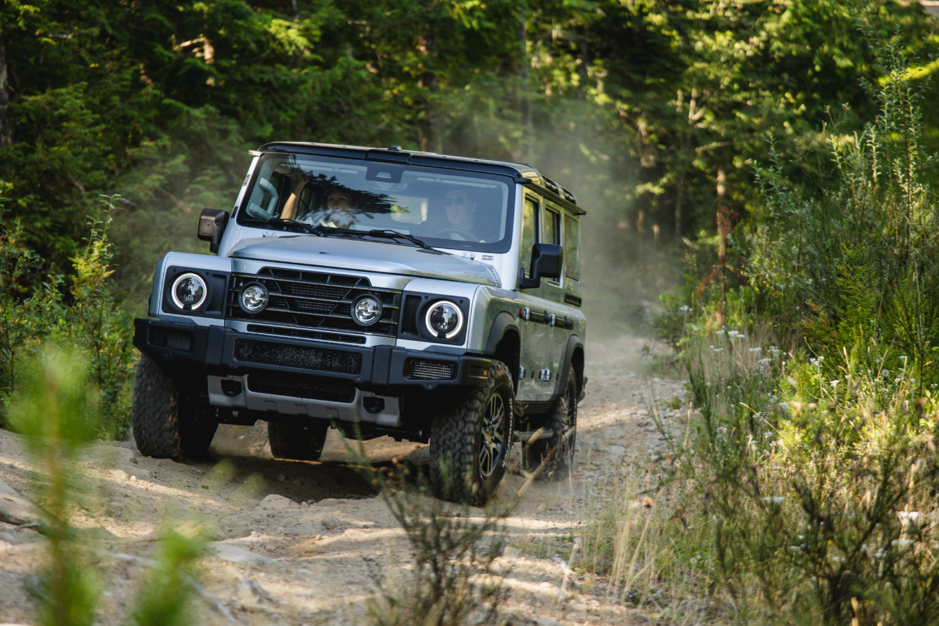 A silver INEOS Grenadier drives up a dirt incline.