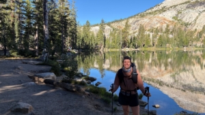 Woman backpacker stands in front of mountain lake