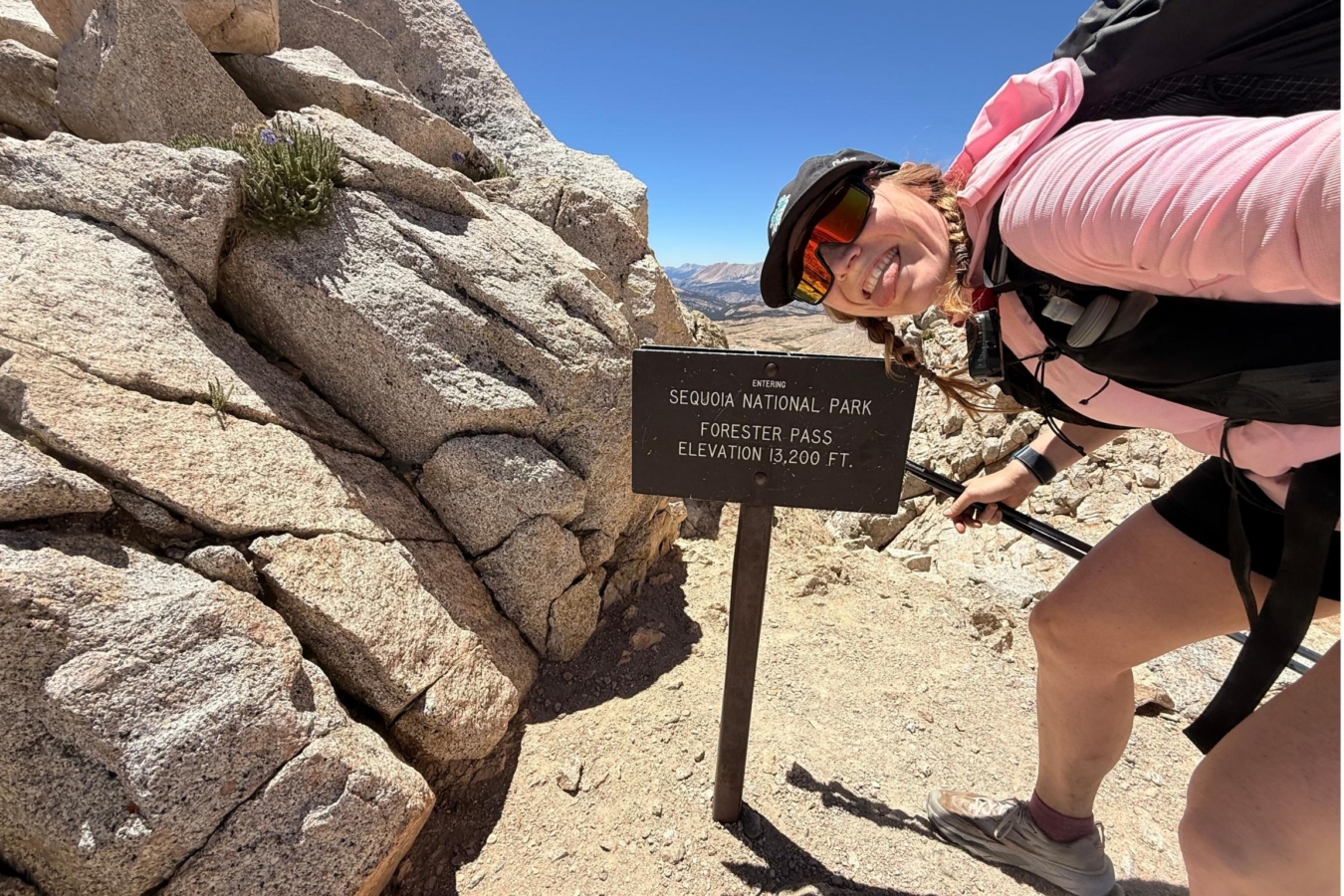 person smiles by trail sign on mountain