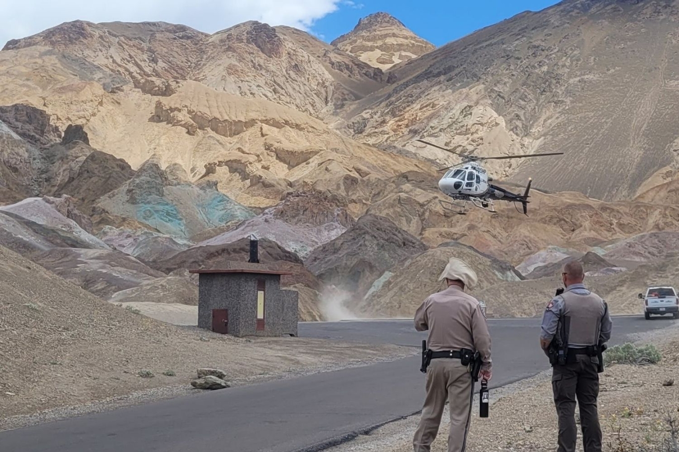 two law enforcement officers look at helicopter in desert