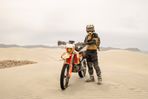 Motorcycle rider standing with a dirt bike among Baja sand dunes