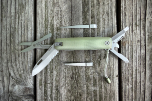 James Brand Helton multitool fully opened with blade, scissors, file, opener, and removable tools displayed on weathered wood