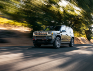a green 2026 Jeep Recon drives on pavement in a forest