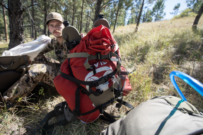 A hunter holding up a backpack frame loaded with elk meat in a game bag.