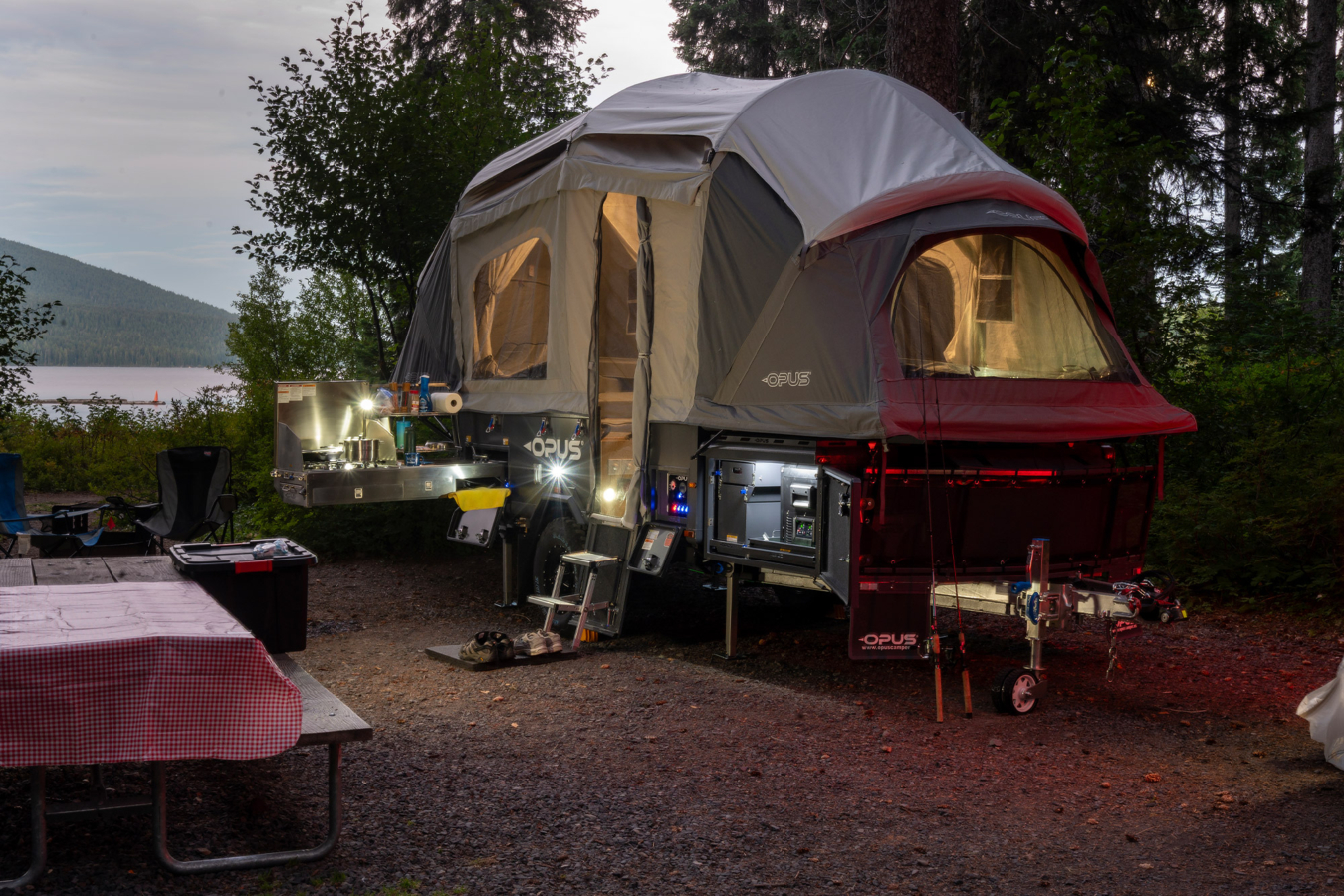 Opus OP4 LE illuminated at a lakeside campsite with the outdoor kitchen open
