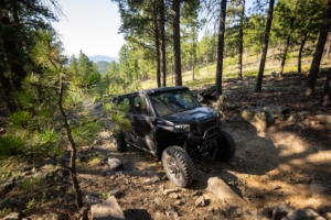 2027 Polaris Xpedition drives through the woods over a rocky trail.