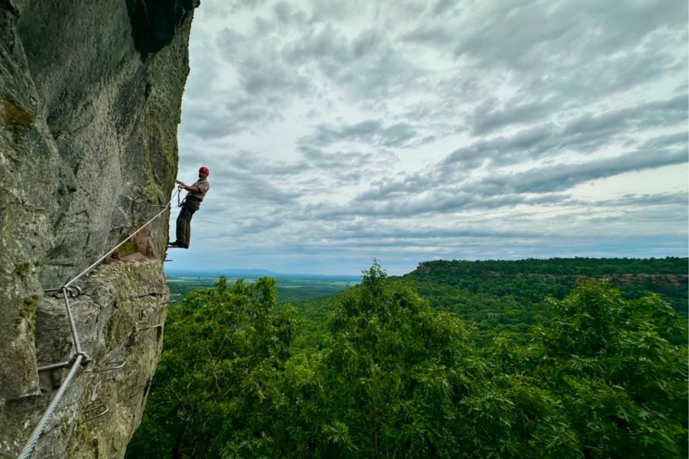 person on via ferrata with open sky and forest in background