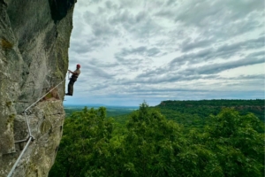 person on via ferrata with open sky and forest in background