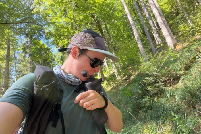 person drinks from water bottle in a pocket in their pack