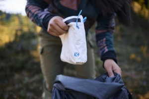 person puts small white pouch into backpack