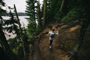 Fastpacker hiking a wooded lakeside trail with poles and a compact running pack