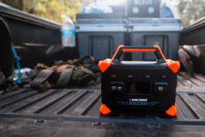 Dark Energy Recon 300 portable power station with orange protective corners sitting in the bed of a pickup truck