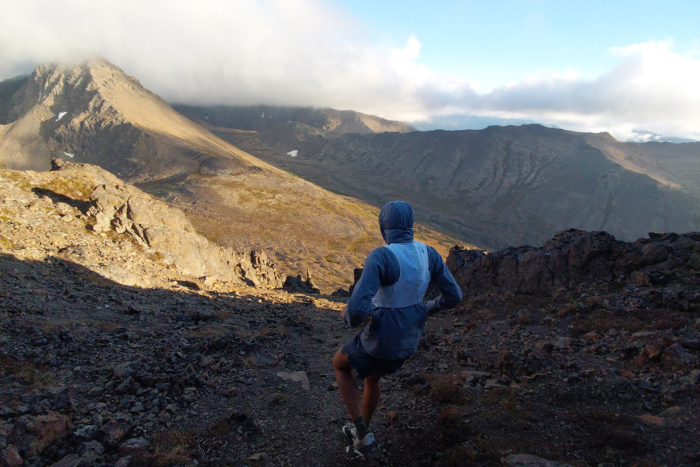 Rear view of a runner descending a rocky mountain trail in a white hydration vest