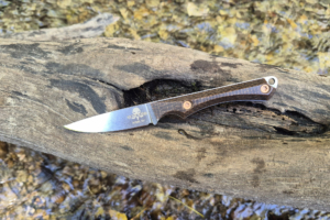 Ice Age Blades Slim Scout fixed blade resting on a log above a creek