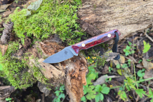 Fang EDC fixed blade knife with a red patterned handle resting on a moss covered log