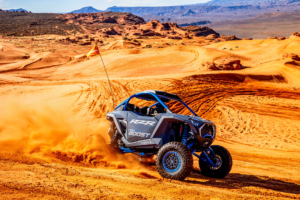 Polaris RZR Pro R Boost kicking up sand while driving across orange desert dunes