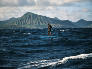 man on SUP foil board in open ocean with Hawaiian island in background