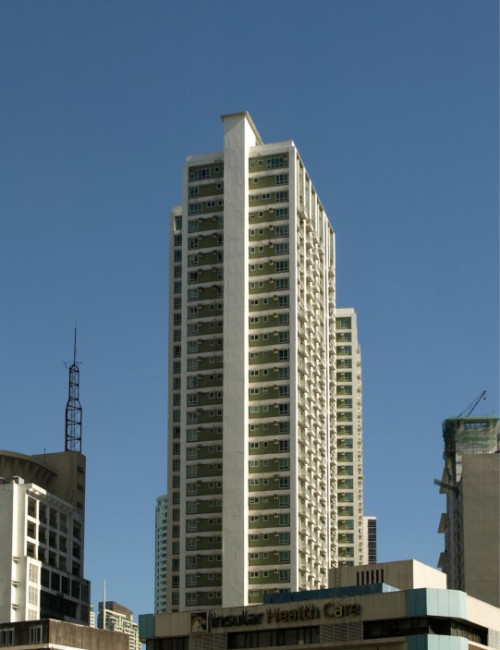 Tall residential building against a clear blue sky, with adjacent structures visible in the foreground.
