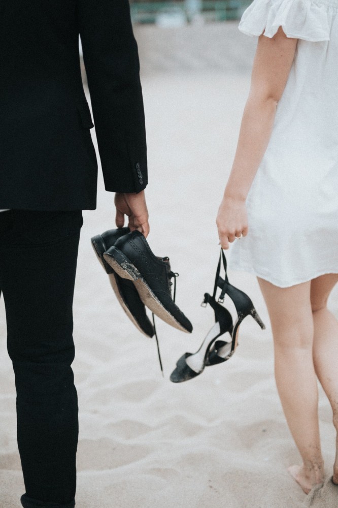 bride and groom holding shoes on beach