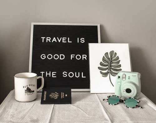 A table with a passport and sign that says, "travel is good for the soul"