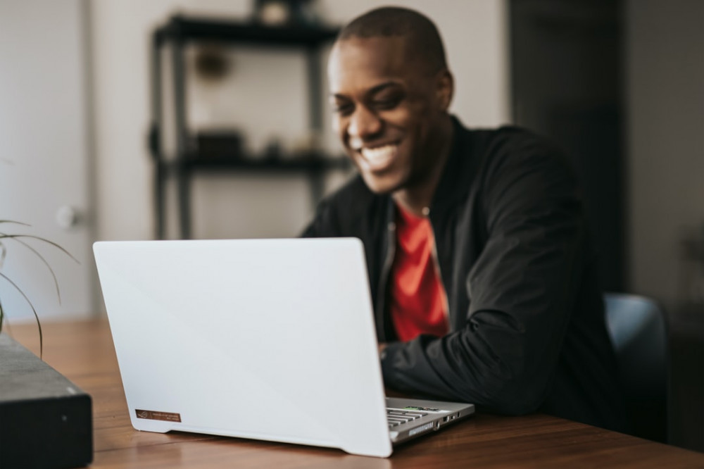 Smiling young man in front of a white laptop Smiling young man in front of a white laptop