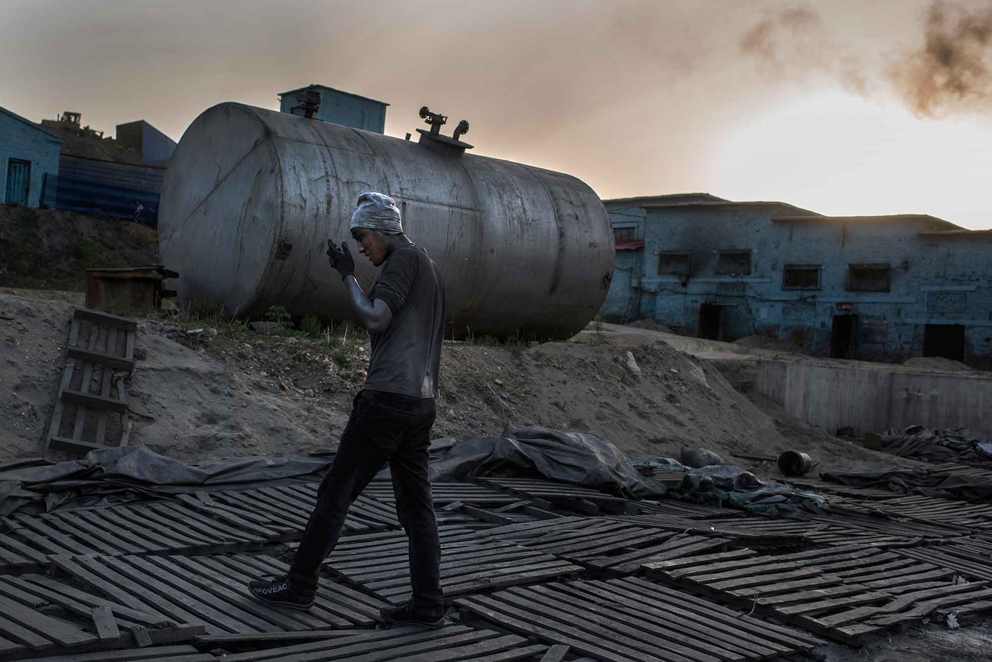 MASHAN, CHINA - MAY 28 A graphite worker walks across the Jin Yang graphite factory in the town of Mashan, China on May 28, 2016. Workers have very little safety equipment at many of the graphite factories. The northeastern province of Heilongjiang is rich in graphite and there are numerous mines and factories in the region. Locals who live in proximity to the factories complain of contaminated air and water affecting their crops and health. The graphite, which is purchased by Samsung and LG Chem, is a key ingredient in lithium batteries for mobile phones and electric cars. (Michael Robinson Chavez/The Washington Post)
