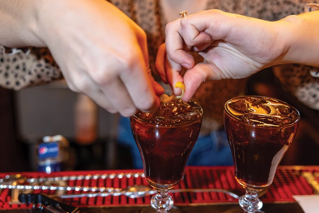Iturriaga rubs the lemon rind on the rim of the glass, twists it, and then places it in the drink.