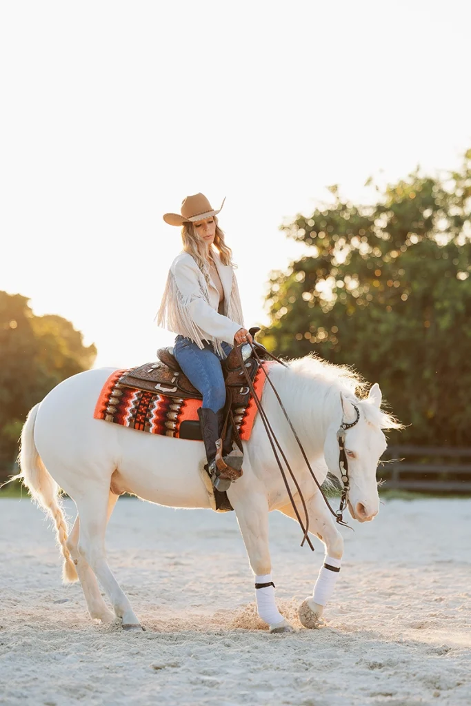 A blonde cowgirl spinning a cremello reining horse.