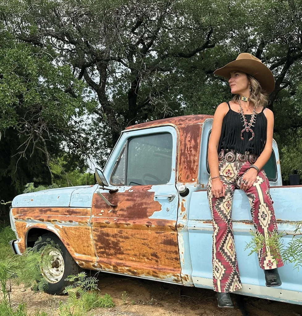 A cowgirl sits on an antique truck.