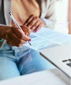 A woman's hand holds a pen as she fills out a form on a glass tabletop next to a laptop computer. Disability attorneys like those at Nash Disability Law can help people wade through all the forms required to get Social Security Disability benefits.