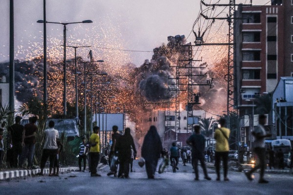 People watch as smoke and flames rise over a building, following Israeli attacks on Deir al-Balah. Israel bombarded the central Gazan city multiple times throughout the year. Gaza, 6 June 2024