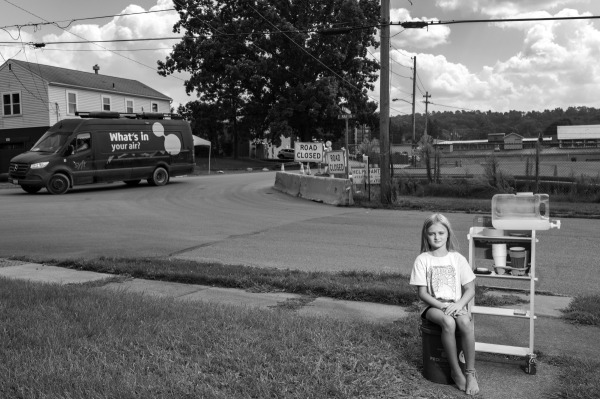 LaBrea Letson (8) sells lemonade made with bottled water outside her grandmother’s home near the derailment site. A van passing by tests the air for hazardous chemicals. East Palestine, Ohio, United States, 18 August 2023