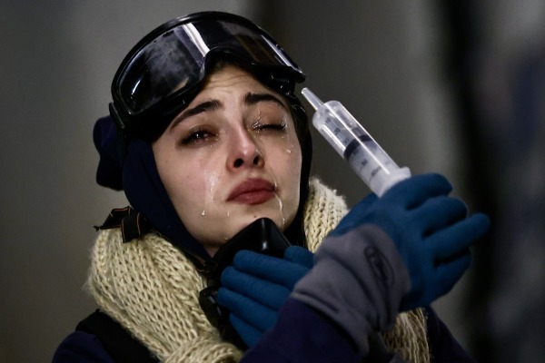 A protester rinses her eyes after police have deployed tear gas. She wears a protective ski mask, respirator, and gardening gloves (to pick up hot gas containers). Tbilisi, Georgia, 7 December 2024