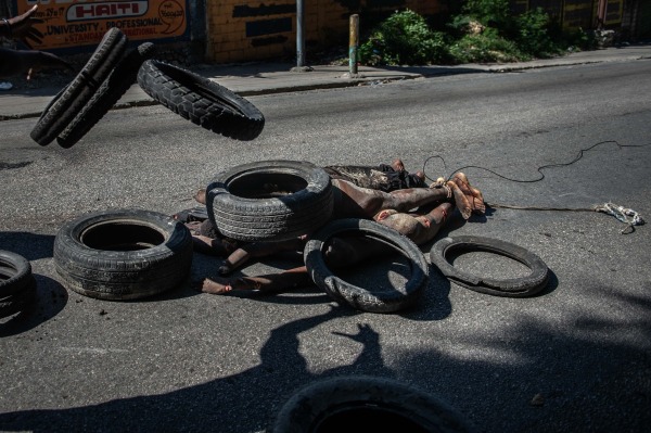 A local resident throws tires on the bodies of suspected gang members killed by police. Pétion-Ville, Port-au-Prince, Haiti, 19 November 2024