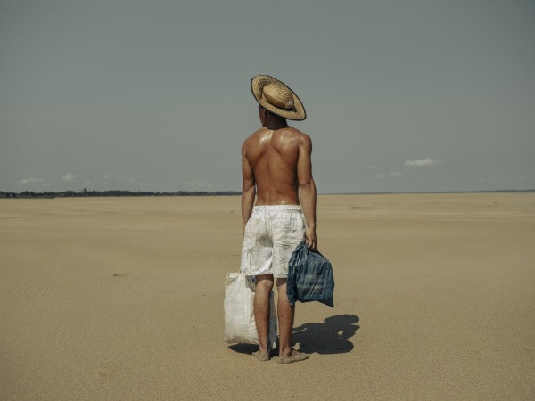 A young man brings food to his mother who lives in the village of Manacapuru. The village was once accessible by boat, but because of the drought, he must walk 2 kilometers along the dry riverbed of the Solimões River to reach her. Amazonas, Brazil, 5 October 2024