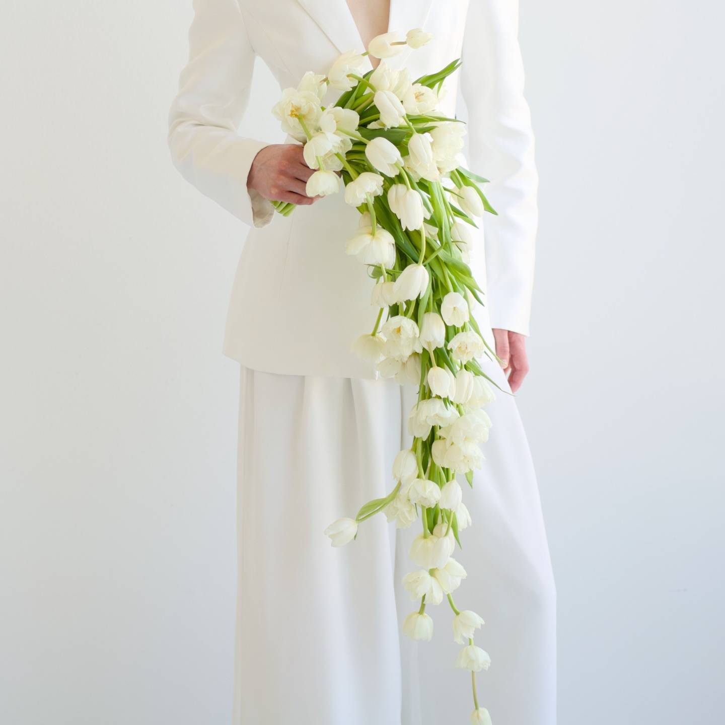 White tulip cascade bouquet held against a white suit