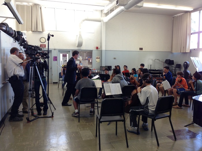Cameraman Rob Englehardt and Director Ty Kim discuss a camera angle as PACO Guest Conductor Scott Krijnen inspires young musicians.