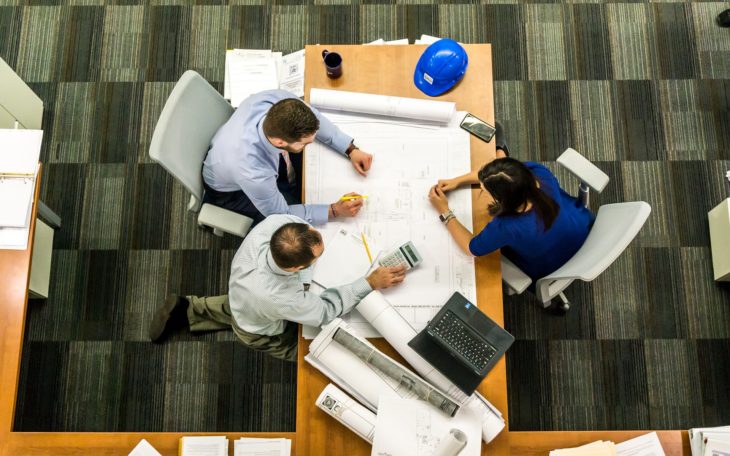 Three people sitting at a desk in a business meeting with paperwork.