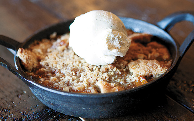 Peach cobbler with a drop-biscuit bottom, bourbon peach filling, and oatmeal streusel topping served with vanilla ice cream topped with bourbon sauce.