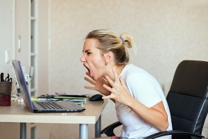 Angry woman screaming at computer screen in disbelief.