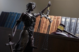 Statue of blindfolded lady of justice in front of shelf of law books and a judge's gavel.