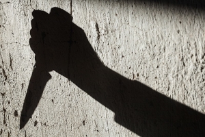 Shadowy image of a hand holding a knife, preparing to stab someone.