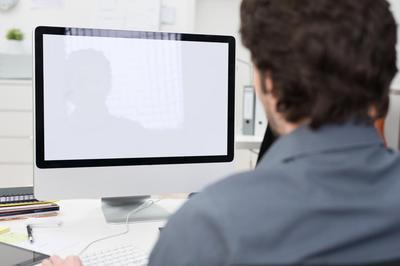 An adult male wearing a collared shirt looking forward at an iMac computer